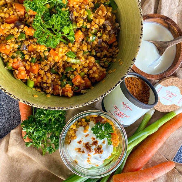 Großer Salat mit roten Linsen, Karotten und Kräutern in einer Schale, daneben Currypulver und eine Joghurtschüssel.