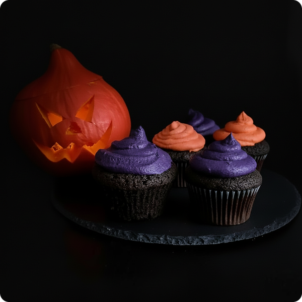 Halloweenská dýně Jack-o'-lantern a pět cupcaků s fialovou a oranžovou polevou na černém podnosu.
