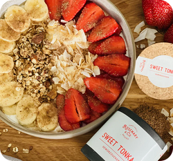 Schale mit Joghurt, Bananen, Erdbeeren, Müsli und Kokosraspeln, umgeben von „Sweet Tonka“ Gewürzzucker auf Holzuntergrund.