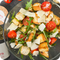 Ein Teller Panzanella-Salat mit Rucola, Tomaten, Croûtons und Parmesanscheiben, daneben Olivenöl und Gewürze.