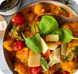 Eine Schüssel Gnocchi in cremiger Sauce, garniert mit Kirschtomaten, Basilikumblättern und Käse.