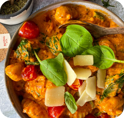 Eine Schüssel Gnocchi in cremiger Sauce, garniert mit Kirschtomaten, Basilikumblättern und Käse.