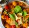 Eine Schüssel Gnocchi in cremiger Sauce, garniert mit Kirschtomaten, Basilikumblättern und Käse.