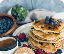 Ein Stapel Blaubeerpfannkuchen mit frischen Blaubeeren, Himbeeren und Gewürzen auf einem Tisch.