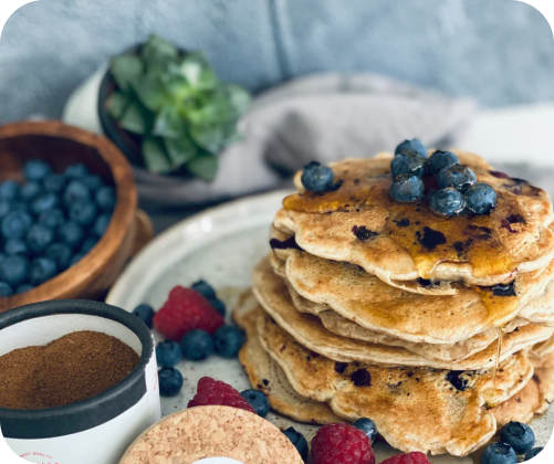 Ein Stapel Blaubeerpfannkuchen mit frischen Blaubeeren, Himbeeren und Gewürzen auf einem Tisch.