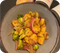 Graue Schale mit Kartoffeln, Rosenkohl, roten Zwiebeln und knusprigem Speck auf schwarzem Untergrund.